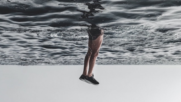 άντρας μέσα στη θάλασσα από τη μέση μέχρι τα πόδια έξω από το νερό φορώντας αθλητικά παπούτσια