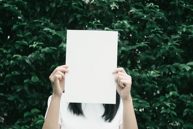Γυναίκα κρατάει ένα λευκό χαρτί μπροστά από το πρόσωπο της